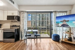 Eine moderne Küche mit Essbereich, ein Balkon mit Blick auf hohe Gebäude und ein Gemälde von einem tropischen Strand.
