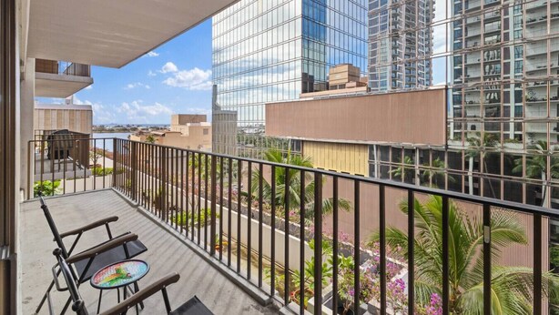 A balcony with a view of a cityscape, including modern buildings and a body of water. - Downtown Honolulu Condo | AC • W/D • Parking (Honolulu)