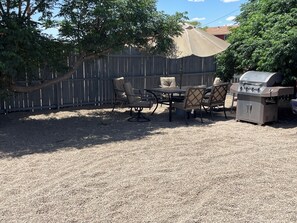 En udendørs terrasse med grill, stole og et bord.