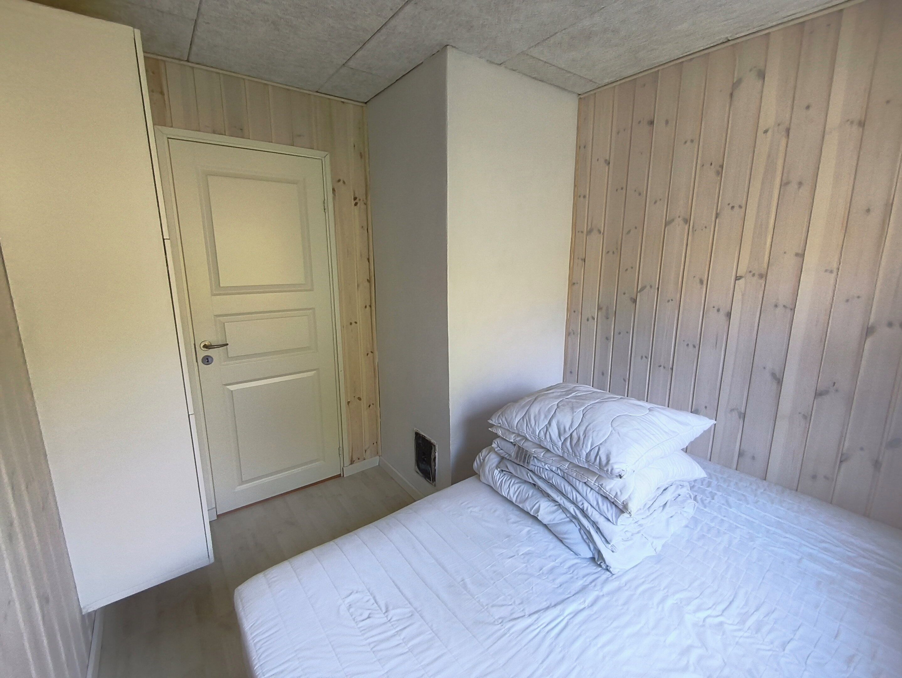 Een slaapkamer met een bed, een deur en houten lambrisering.