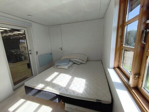 A small bedroom with a bed, a window, and a door leading to a kitchen. - Renovated holiday home with hot tub Marielyst (Væggerløse)