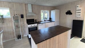 A compact kitchen with wooden paneling, a built-in oven, a white refrigerator, and a black countertop.