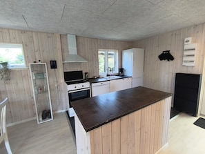 Kompakti keittiö, jossa on puupanelointi, sisäänrakennettu uuni, valkoinen jääkaappi ja musta työtaso.