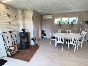 A room with a fireplace, a dining table with chairs, a window with plants, and a door. - Renovated holiday home with hot tub Marielyst (Væggerløse)