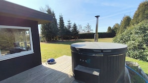 A hot tub on a wooden deck with a view of a grassy yard and trees.