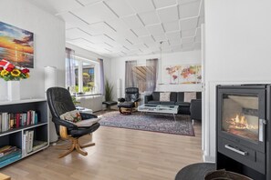 Un salon moderne avec une cheminée, un fauteuil en cuir noir, une bibliothèque et une grande fenêtre.