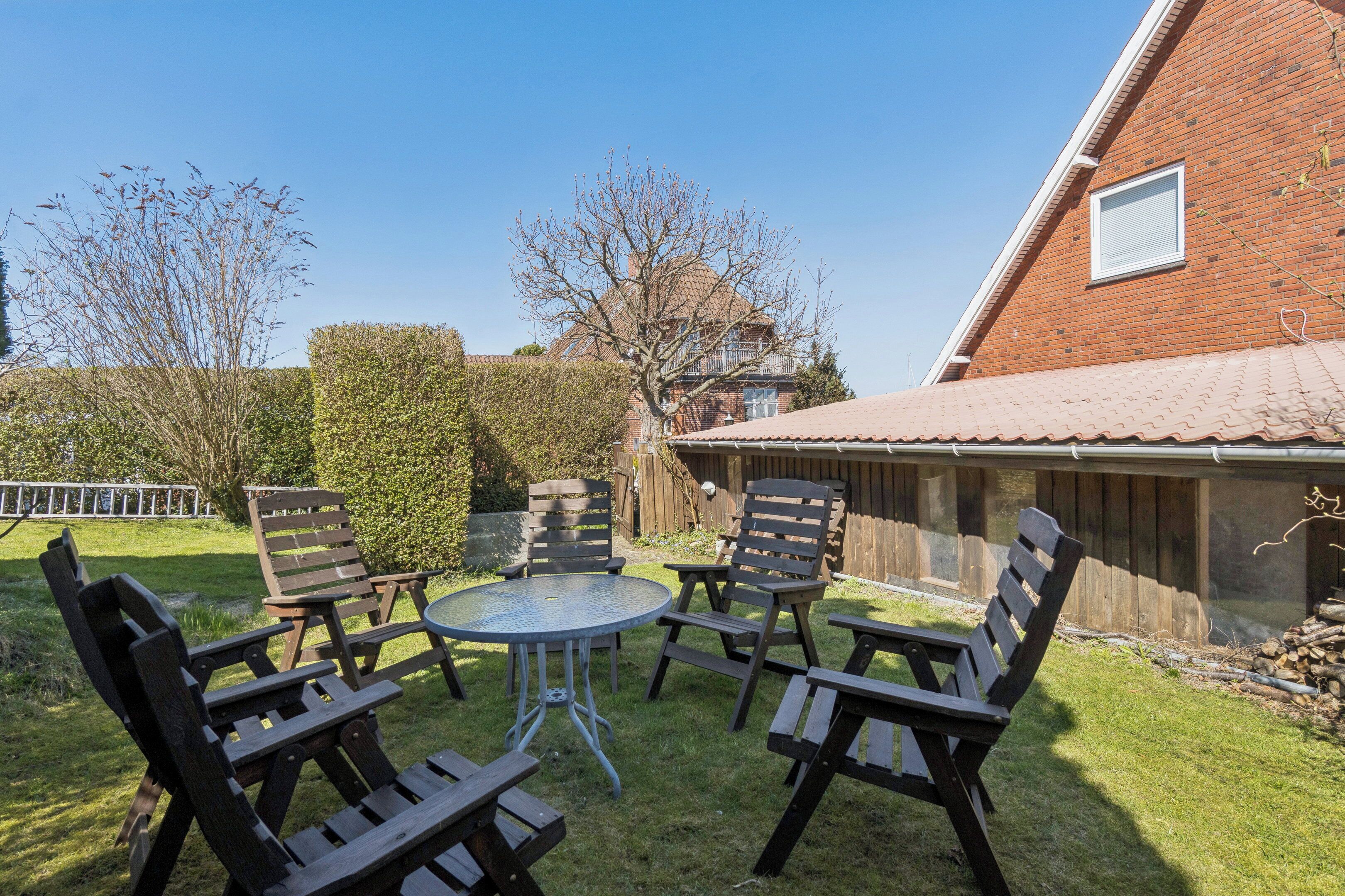 A patio with wooden chairs and a table, a brick building, and a clear sky.
