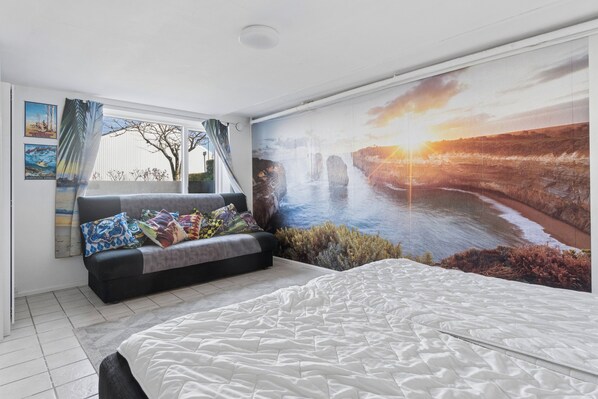 Un dormitorio con cama, sofá, un ventanal grande y un mural de un paisaje.