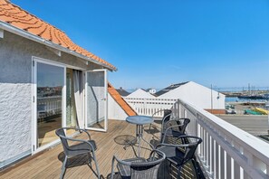 Un balcón con sillas de mimbre y una mesa, puerta corrediza de vidrio y vista al puerto deportivo.