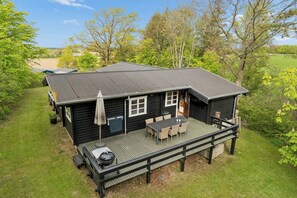 Eine Hütte mit einer Terrasse, Sitzgelegenheiten im Freien und Grillplatz.