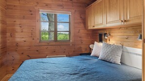 Een houten slaapkamer met een bed, een raam en inbouwmeubels.