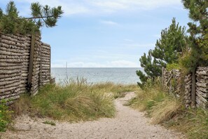 A sandy path leading to a body of water, surrounded by natural vegetation and a stone wall. - Family-friendly beachside holiday home (Nykøbing Sj)