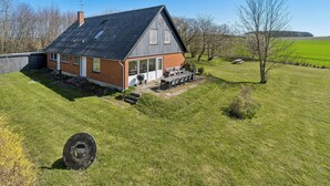 A house with a sloped roof, a chimney, a large window, and a patio with outdoor furniture. - Holiday Charm on Bornholm’s South Coast (Aakirkeby)