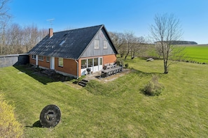A house with a sloped roof, a chimney, a large window, and a patio with outdoor furniture. - Holiday Charm on Bornholm’s South Coast (Aakirkeby)