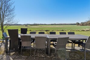 An outdoor dining area with a table and chairs, a view of a green field, and a tree. - Holiday Charm on Bornholms South Coast (Aakirkeby)
