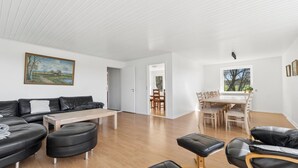 A modern living room with a sectional sofa, ottomans, a wooden coffee table, and a dining area with a table and chairs. - Holiday Charm on Bornholm’s South Coast (Aakirkeby)