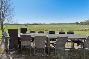An outdoor dining area with a table and chairs, a view of a green field, and a tree.