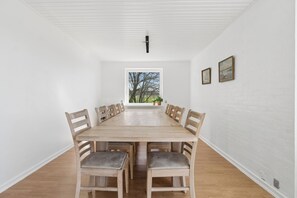 Une salle à manger avec une longue table en bois, six chaises et une fenêtre donnant sur des arbres.