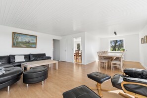 A modern living room with a sectional sofa, ottomans, a wooden coffee table, and a dining area with a table and chairs. - Holiday Charm on Bornholms South Coast (Aakirkeby)