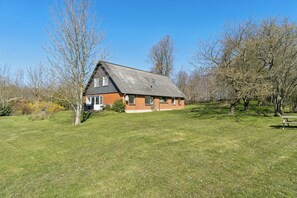 Une maison avec un toit en pente, entourée d’une pelouse et d’arbres.
