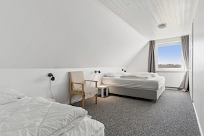 A bedroom with a bed, a chair, a small table, and a window with curtains.