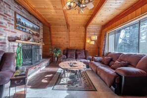 Ein rustikales Holzhaus-Interieur mit Kamin, Ledersofas, einem runden Couchtisch und einem großen Fenster.