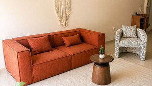 A living room with a sectional sofa, a round coffee table, a macrame wall hanging, and a patterned armchair. - 10-Mins from Cairo Airport, Garden Oasis (Cairo Governorate)