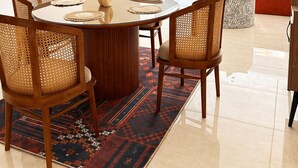 A modern living room with a dining area, featuring a round table, wicker chairs, a patterned rug, and a view of the outside. - 10-Mins from Cairo Airport, Garden Oasis (Cairo Governorate)