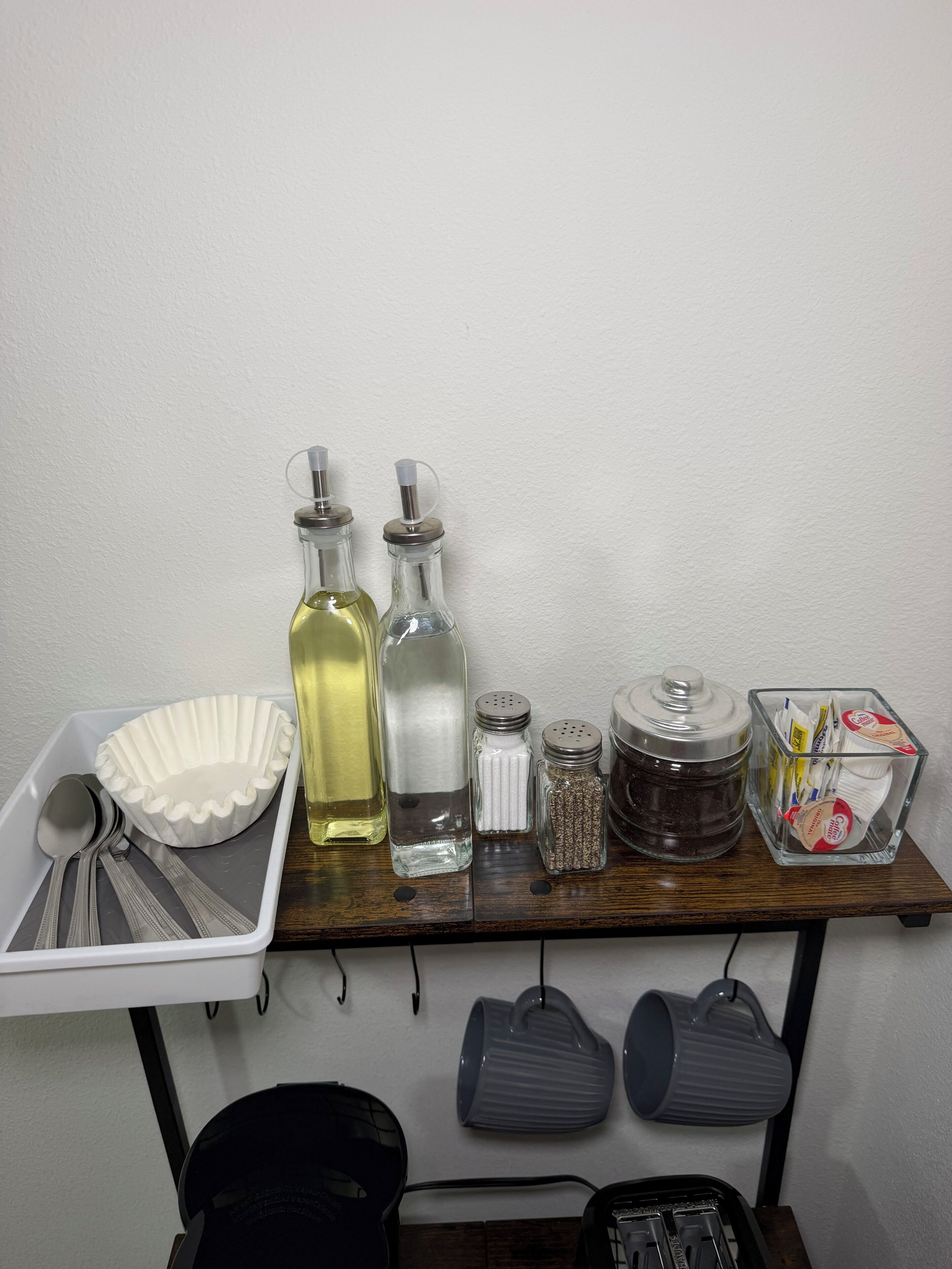 Un plan de travail de cuisine sur lequel on trouve divers objets, notamment un bol blanc, deux bouteilles, un salier, un poivrier, un récipient à sucre et une boîte de sachets de thé.