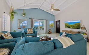 A spacious living room with a large sectional sofa, a ceiling fan, and a large window offering a view of the outdoors.