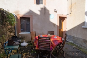 Eine Terrasse im Freien mit einem für zwei Personen gedeckten Tisch, umgeben von Stühlen, einem Grill und einem kleinen Tisch mit einem Korb.