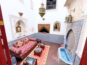 Ein traditionelles marokkanisches Interieur mit einer gemusterten Couch, einem kleinen Tisch, einer dekorativen Laterne und einer Kachelwand.