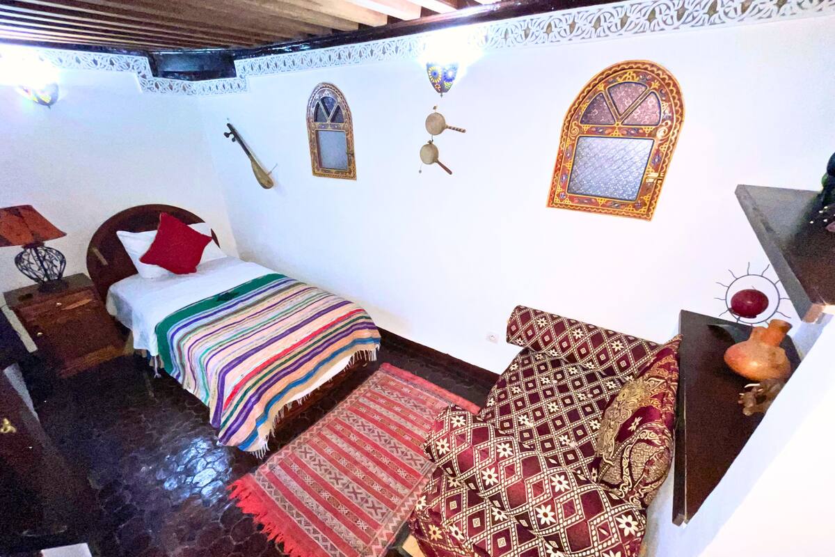 A room with a bed, a nightstand, a wall-mounted TV, and a patterned rug.