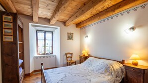 A bedroom with a wooden bed, a nightstand, a chair, a window with curtains, and a wooden wardrobe. - Grand Gîte La Panouse en Margeride (LA PANOUSE)