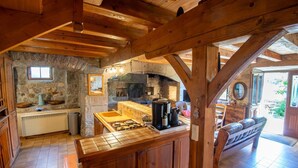 A rustic kitchen with stone walls, wooden beams, and a stone fireplace. - Grand Gîte La Panouse en Margeride (LA PANOUSE)