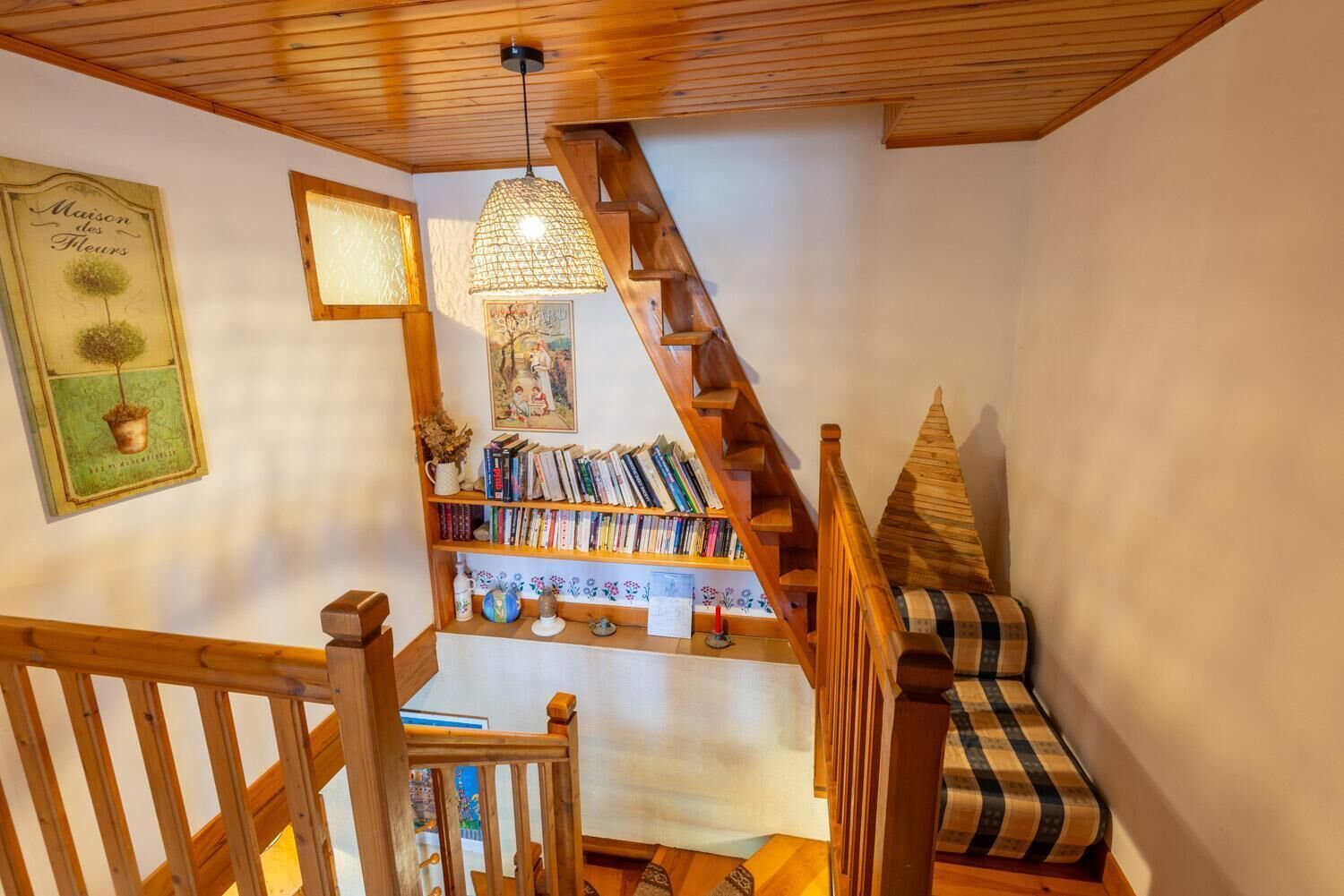 A wooden staircase with a bookshelf, a hanging light fixture, and a decorative wall piece.
