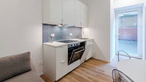 Une cuisine compacte avec des meubles blancs, un four encastré et une fenêtre donnant sur un mur de briques.