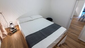 Une chambre à coucher avec un lit, une table de chevet avec une lampe et une porte donnant sur une autre pièce.