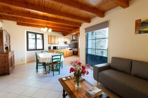 A spacious living area with a sofa, a dining table with chairs, a kitchen area, and a large window with a view. - L'OUSTAL DE LUCIE - SAINT SATURNIN (SAINT SATURNIN)