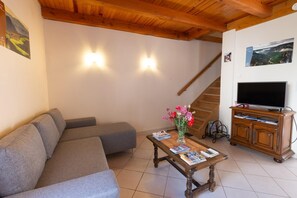 A living room with a sofa, a coffee table with magazines, a TV on a wooden stand, and a staircase. - L'OUSTAL DE LUCIE - SAINT SATURNIN (SAINT SATURNIN)