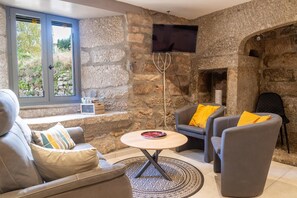 Ein gemütliches Wohnzimmer mit Steinwänden, Kamin, Flachbildfernseher und bequemen Sitzmöglichkeiten.