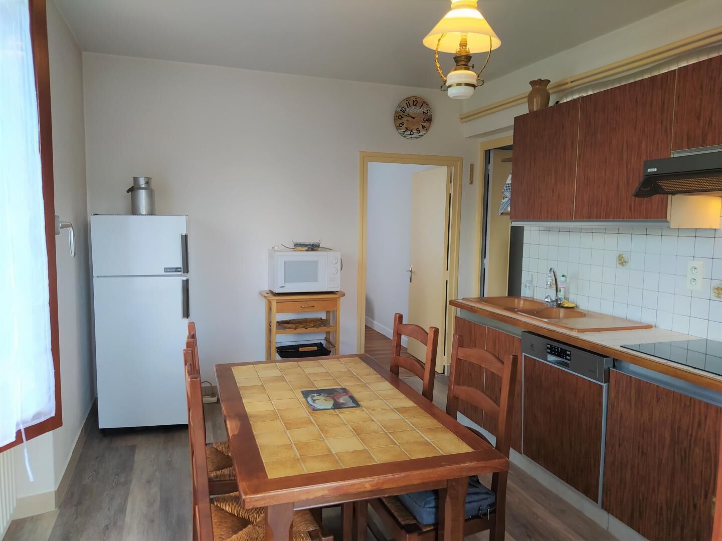 Cocina compacta con refrigerador, microondas, mesa de madera, sillas y lavavajillas.