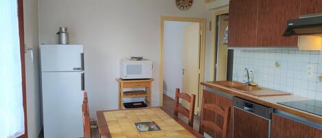 Cocina compacta con refrigerador, microondas, mesa de madera, sillas y lavavajillas.