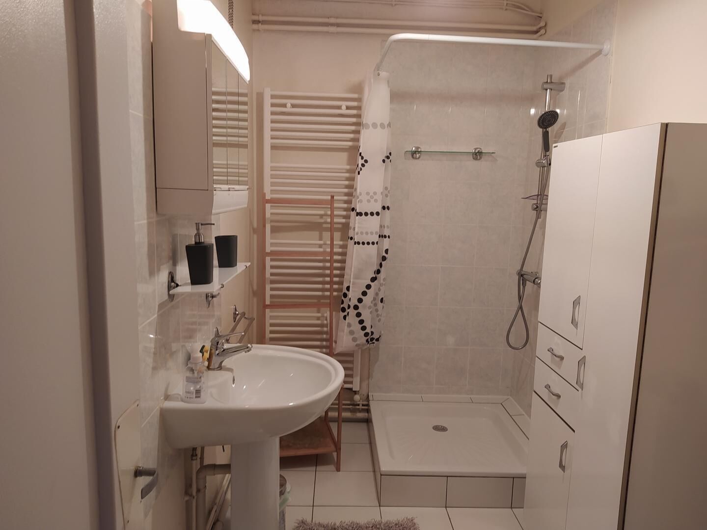 A bathroom with a sink, mirror, towel rack, shower, and storage cabinets.