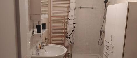A bathroom with a sink, mirror, towel rack, shower, and storage cabinets.