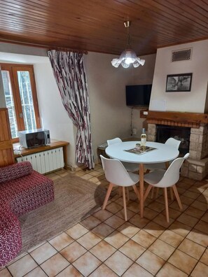 Ein gemütliches Wohnzimmer mit Kamin, einem Esstisch mit Stühlen, einer Couch, einem Fernseher und einem gemusterten Vorhang.