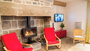 Ein Steinkamin mit darüber montiertem Fernseher, zwei rote Sessel, ein Korbsessel und eine rote Kommode.