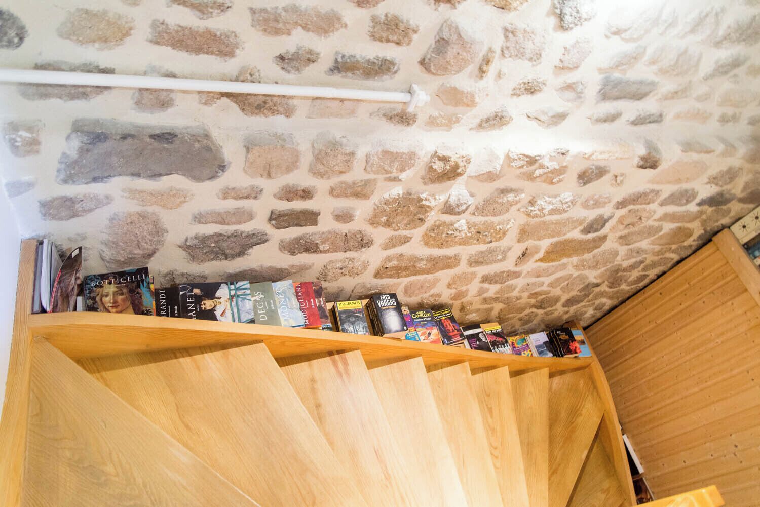 Una habitación con techo de piedra, escalera de madera y una estantería llena de libros.