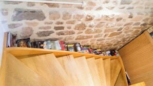 Ein Zimmer mit Steindecke, einer Holztreppe und einem Bücherregal mit verschiedenen Büchern.
