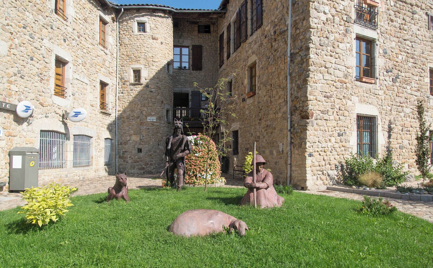 A stone building with a courtyard, statues, and a pig lying on the grass.
